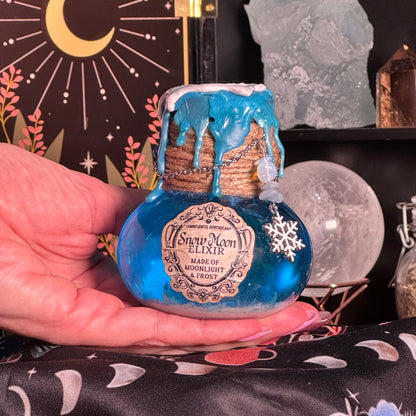 Blue elixir bottle labeled 'Snow Moon Elixir' held in a hand with a mystical background.
