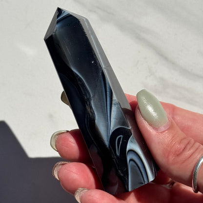 Marbled black and gray onyx tower held by a hand on a white background