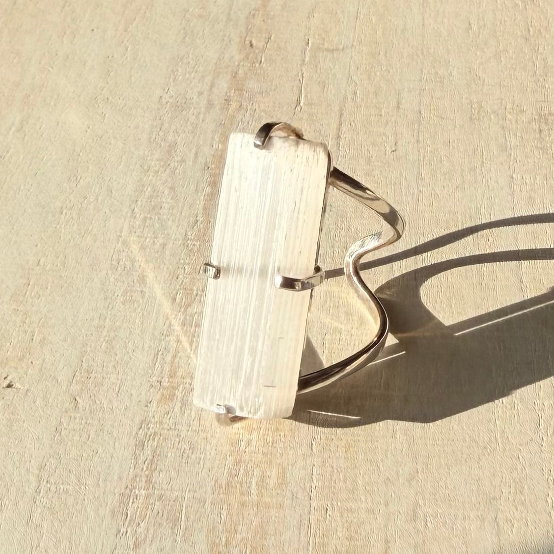 Silver selenite ring with a rectangular stone on a beige surface