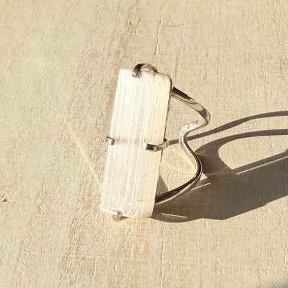 Silver selenite ring with a rectangular stone on a beige surface