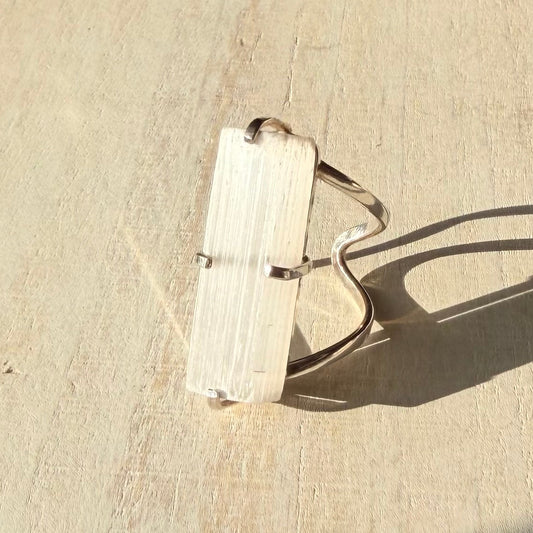 Silver selenite ring with a rectangular stone on a beige surface