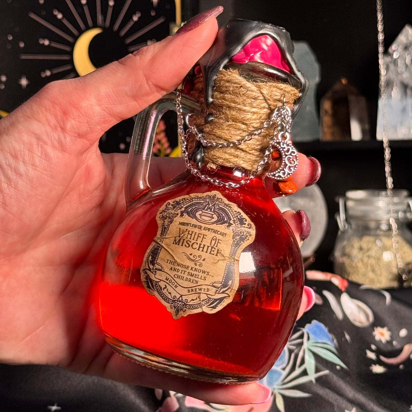 Hand holding a bottle labeled 'Whiff of Mischief' with a mystical background.